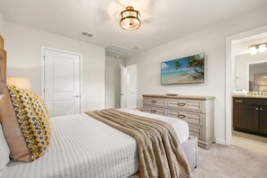 A bedroom with a bed, a dresser, a painting of a beach, and a hallway leading to a bathroom. - Halloween Game Room! Sleeps 10 Windsor Cay - 1273 ER (Clermont)