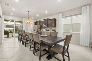 A modern kitchen with dark cabinetry, a central island, and a dining area with a long table and chairs. - Halloween Game Room! Sleeps 10 Windsor Cay - 1273 ER (Clermont)