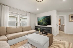 A living room with a beige sectional sofa, a coffee table, and a flat-screen TV mounted on a wall. - Halloween Game Room! Sleeps 10 Windsor Cay - 1273 ER (Clermont)