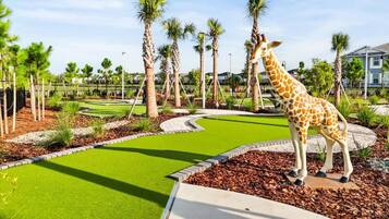 A giraffe statue in a landscaped area with palm trees and a curved pathway.