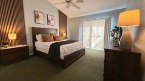 Ein Hotelzimmer mit einem Bett, Nachttischen, einem Schreibtisch, einer Lampe und einem Deckenventilator.