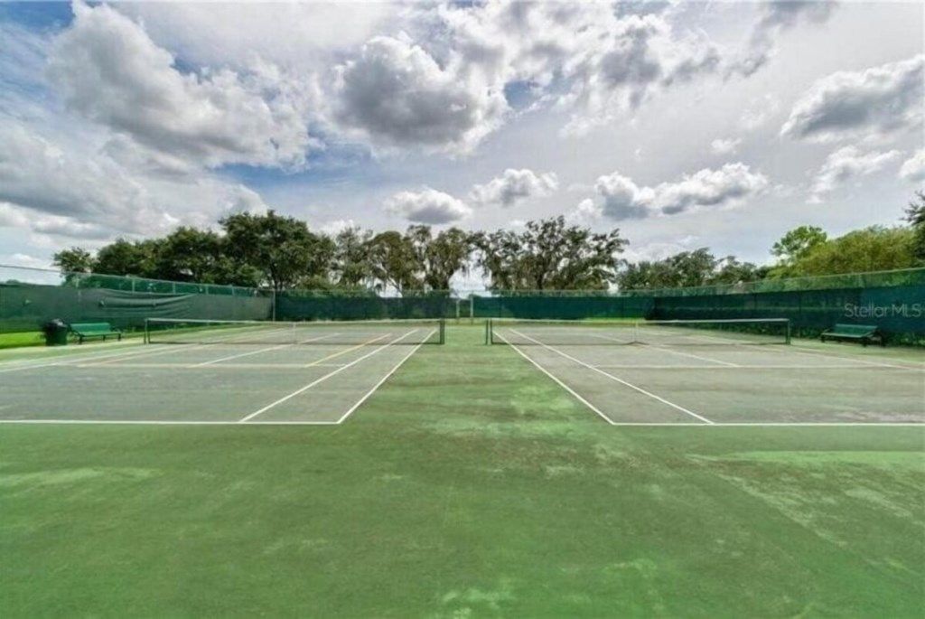 Ein Tennisplatz im Freien mit Netz, umgeben von Bäumen und blauem Himmel.