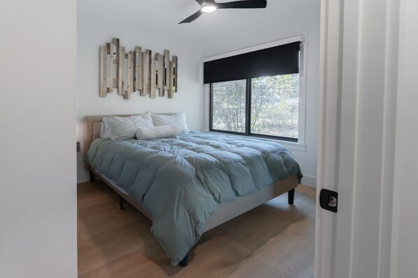 A bedroom with a bed, a ceiling fan, a window with a black blind, and a wall-mounted light fixture.