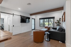 A modern living room with a sofa, armchairs, a coffee table, and a TV mounted on the wall.