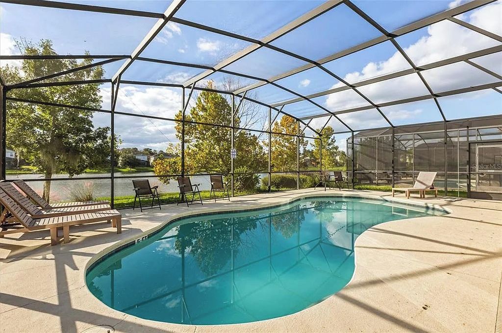 Une piscine entourée de parois en verre, agrémentée de chaises longues et offrant une vue sur les arbres.