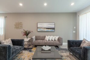 Un salón con un sofá gris, dos sillones, una mesita de centro con un objeto decorativo y un cuadro en la pared.
