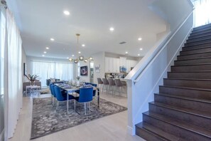 Una cocina moderna con armarios blancos, un comedor con sillas azules y una escalera.