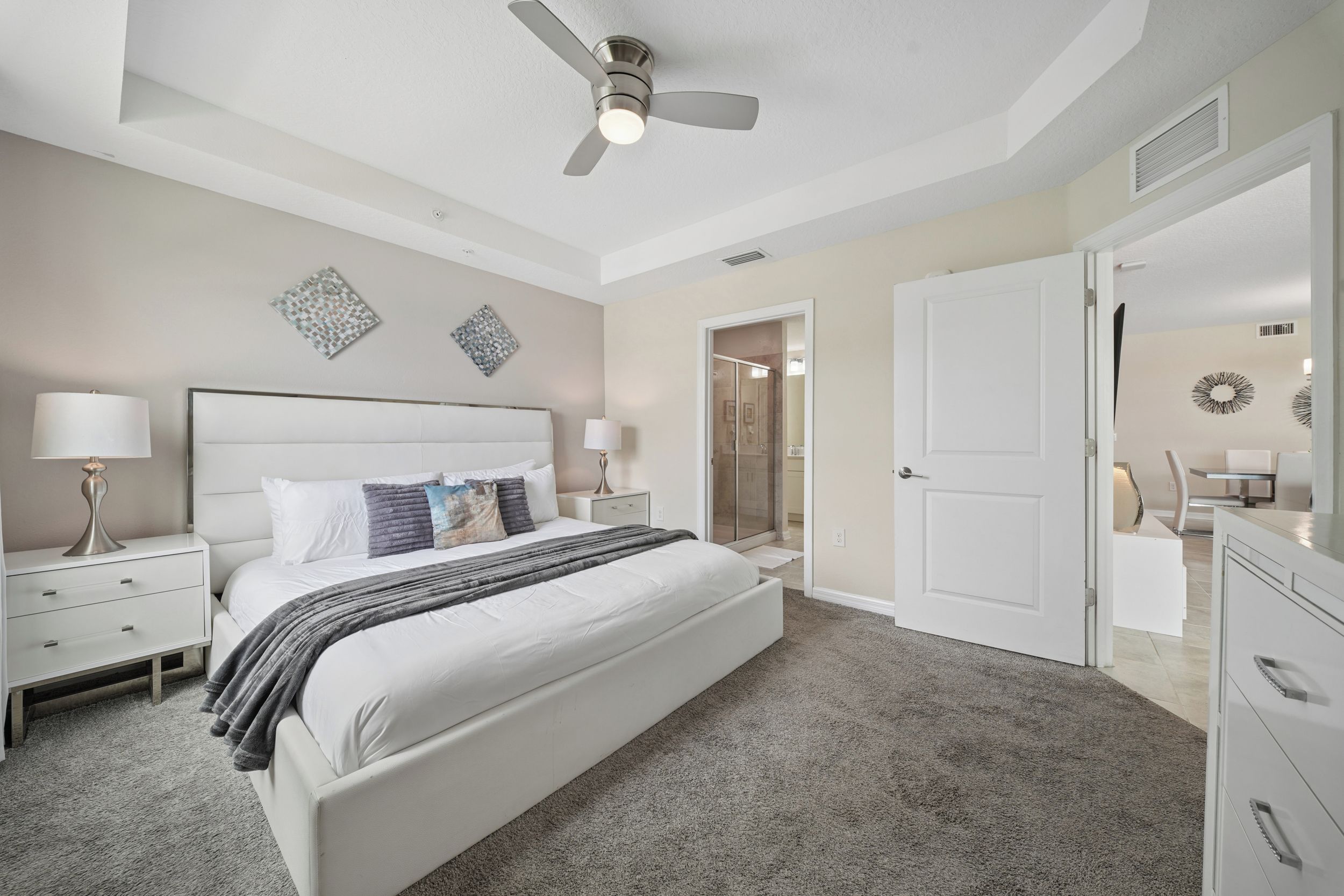 A bedroom with a bed, bedside tables, a ceiling fan, and a door leading to a bathroom.