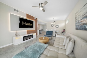 A modern living room with a flat-screen TV, a fireplace, a ceiling fan, and a blue armchair. - Relaxing Storey Lake Escape 3 BD/ 2 BA (3120-201PC) (Kissimmee)