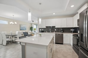 A modern kitchen with white cabinets, a stainless steel refrigerator, and a dining area with a table and chairs. - Relaxing Storey Lake Escape 3 BD/ 2 BA (3120-201PC) (Kissimmee)