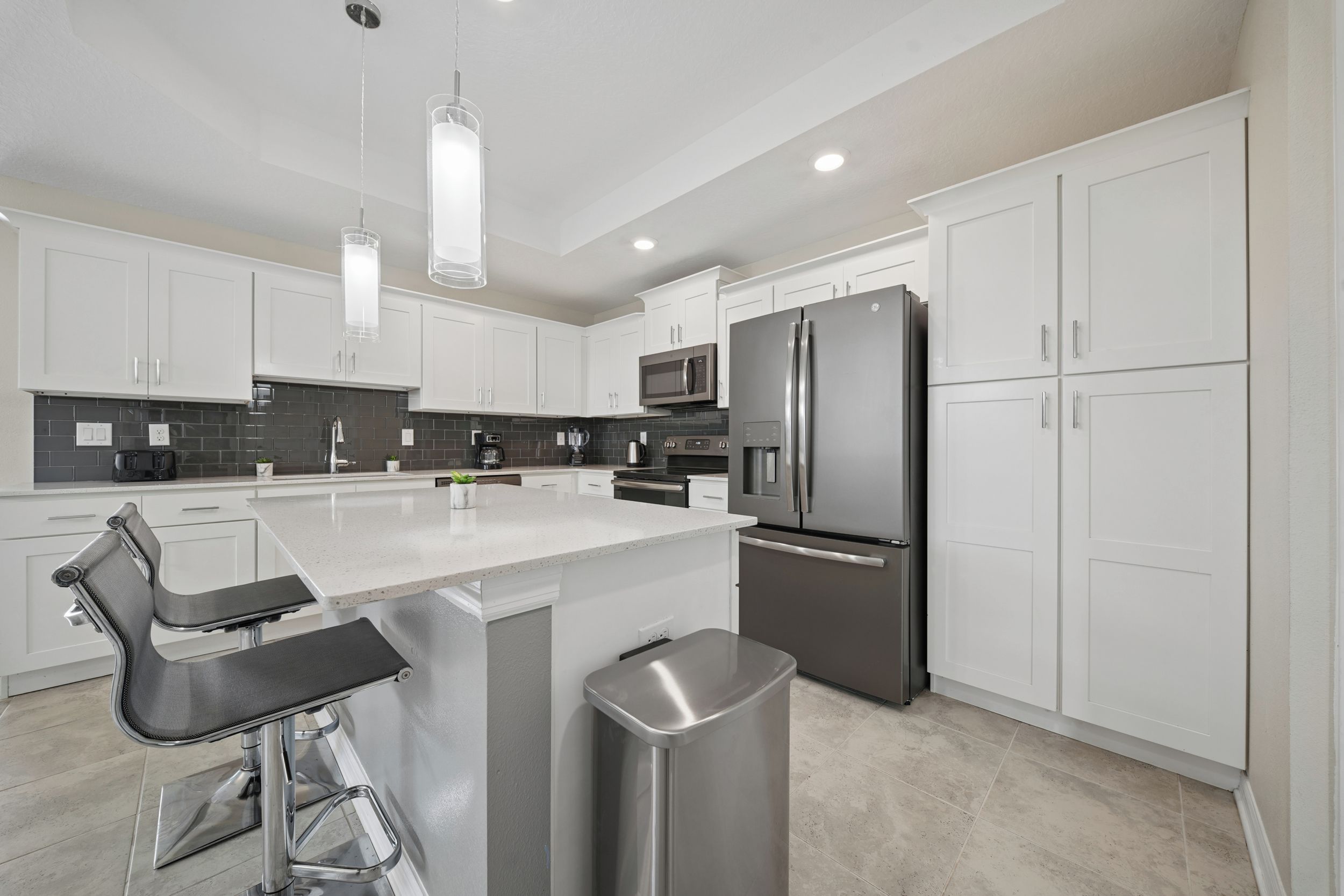 Una cocina moderna con muebles blancos, electrodomésticos de acero inoxidable y una isla central con taburetes de bar.