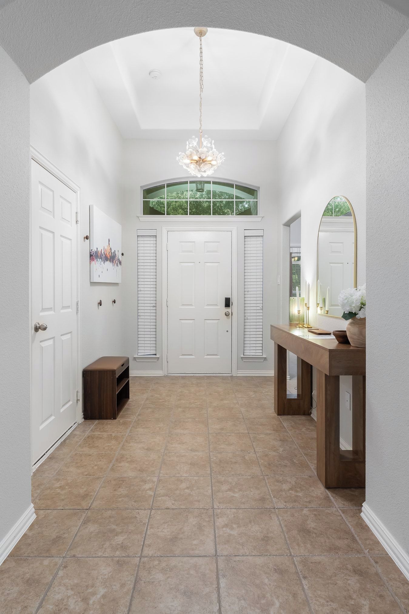 A spacious hallway with a high ceiling, a chandelier, a large mirror, and a wooden console table.