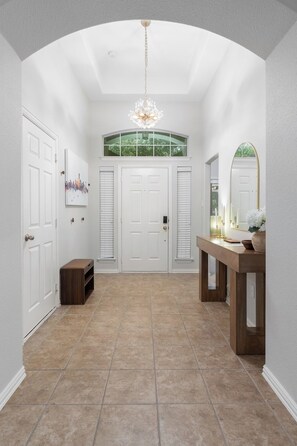 A spacious hallway with a high ceiling, a chandelier, a large mirror, and a wooden console table. - Family-Friendly Frisco Home Near Universal & PGA (Frisco)