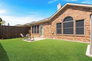 A residential house with a brick exterior, a well-maintained lawn, and a patio area with outdoor furniture.