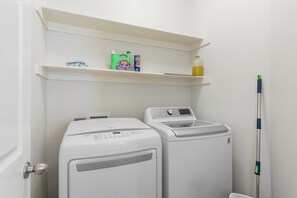A laundry area with a front-loading washer and dryer, a shelf with cleaning supplies, and a mop leaning against the wall.