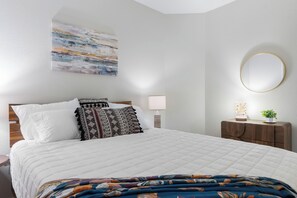 A bedroom with a bed, pillows, a bedside table with a lamp, a small plant, and a wall-mounted mirror. - Family-Friendly Frisco Home Near Universal & PGA (Frisco)
