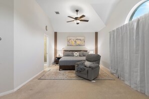 A bedroom with a bed, a chair, a ceiling fan, a painting, and a window with curtains. - Family-Friendly Frisco Home Near Universal & PGA (Frisco)