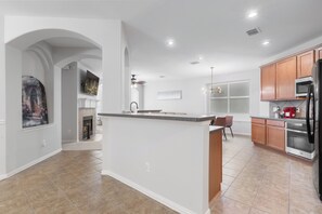 A modern kitchen with a central island, wooden cabinets, and a built-in oven. - Family-Friendly Frisco Home Near Universal & PGA (Frisco)