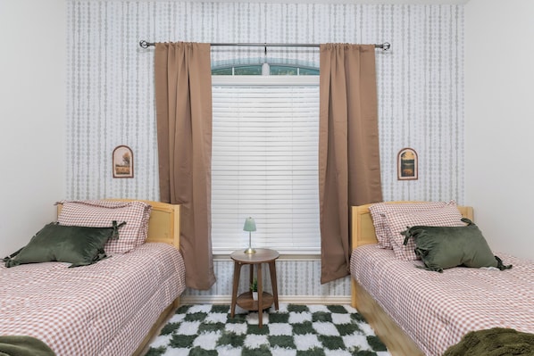 A room with two beds, a small table, and a window with curtains.