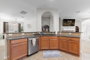A modern kitchen with wooden cabinets, a stainless steel dishwasher, and a granite countertop. - Family-Friendly Frisco Home Near Universal & PGA (Frisco)