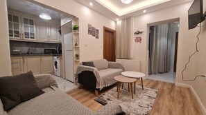 A compact living space with a kitchenette, a sofa, a small table, and a radiator.