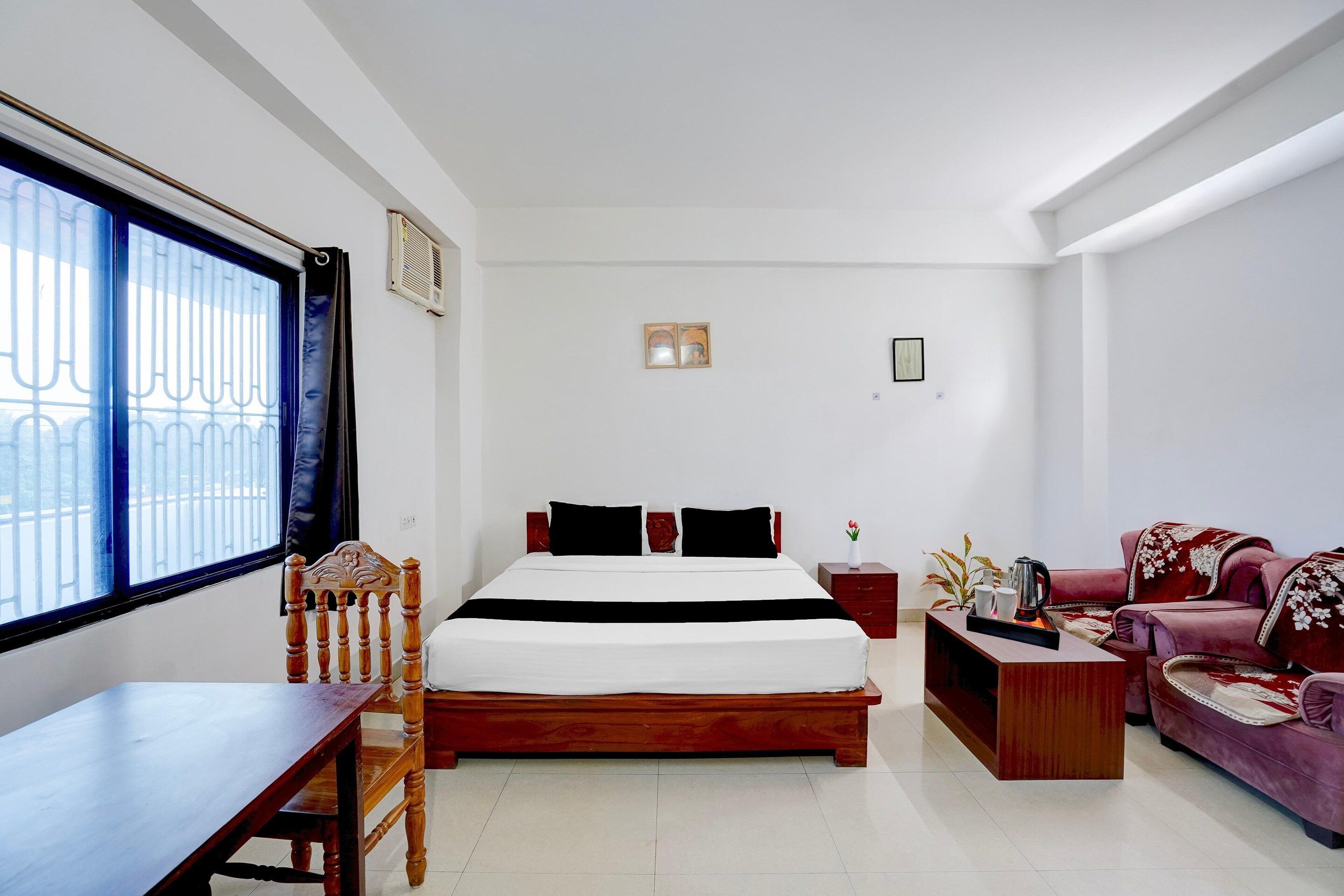 A hotel room with a bed, a wooden chair, a small table, a sofa, and a window with bars.