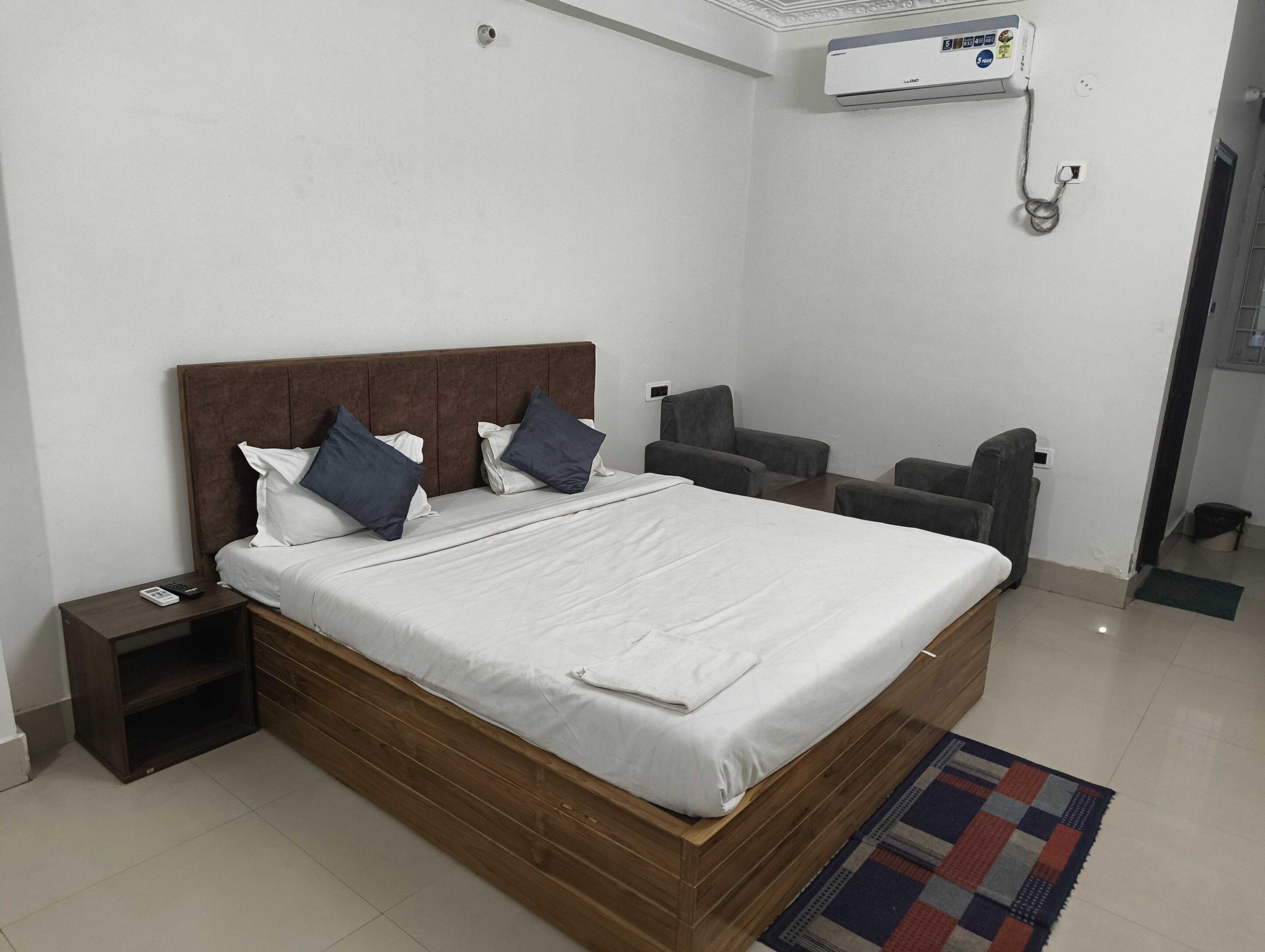 A bedroom with a bed, bedside tables, a chair, a small table, and a wall-mounted air conditioner.