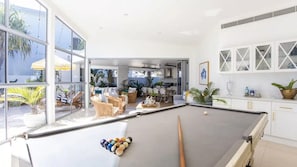 A spacious indoor area with a pool table, comfortable seating, and large windows offering views of the outdoors. - Paradise @ Salt - Private pool, pool table, close to beach & cafes (Kingscliff)
