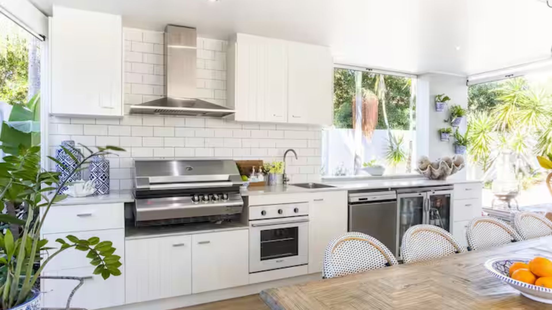 A modern kitchen with white cabinetry, stainless steel appliances, and a dining area with a wooden table and wicker chairs.
