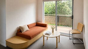 A modern living room with a curved sofa, a small round table, and a wicker chair. - Creekside Beach house (Kingscliff)