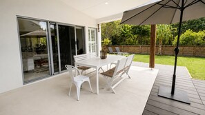 Une terrasse avec une table et des chaises blanches, une plateforme en bois et une vue sur un jardin.