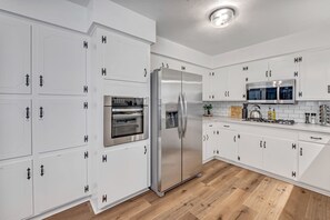 A modern kitchen with white cabinetry, stainless steel appliances, and a wooden floor. - Spacious 5BR Retreat, Private Pool + Outdoor Game Room (Pasadena)