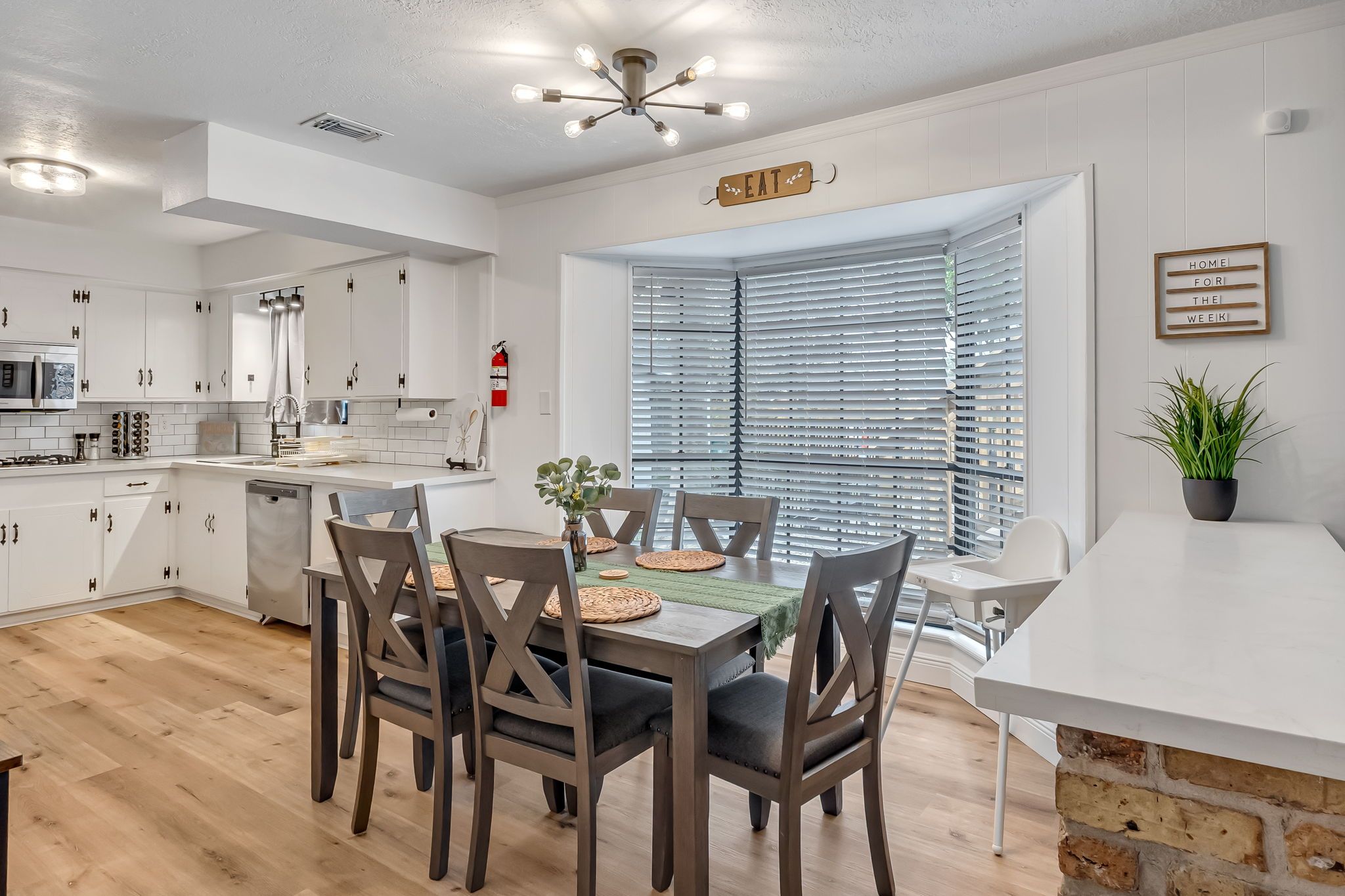 A modern kitchen with white cabinets, a dining area with a table and chairs, and a window with blinds.