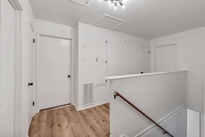 A hallway with white walls, a wooden floor, and a staircase with a wooden handrail. - Spacious 5BR Retreat, Private Pool + Outdoor Game Room (Pasadena)