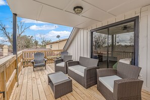 A covered outdoor deck with wicker furniture, a wooden deck, and a glass door leading to a patio. - Spacious 5BR Retreat, Private Pool + Outdoor Game Room (Pasadena)