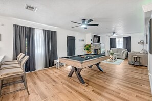 A room with a pool table, a sofa, a television, and a ceiling fan. - Spacious 5BR Retreat, Private Pool + Outdoor Game Room (Pasadena)