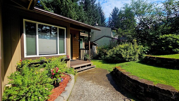 A residential house with a front porch, a small garden with flowers, and a well-maintained lawn.