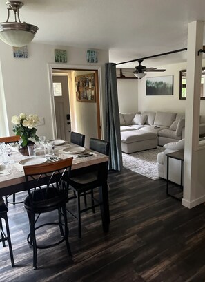 Un coin repas avec une table dressée pour quatre personnes, un canapé et un ventilateur de plafond en arrière-plan.