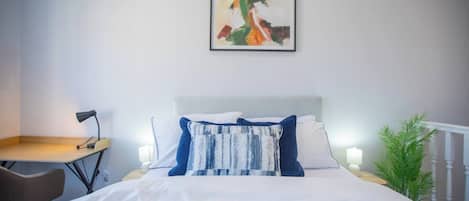Une chambre d’hôtel comprenant un lit, un bureau, une chaise, une table de chevet avec une lampe et un tableau accroché au mur.