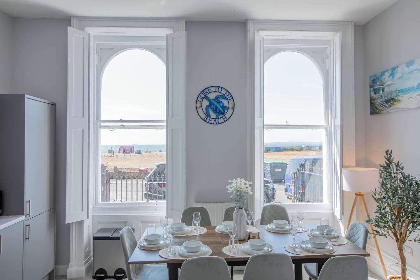 Een eetkamer met uitzicht op het strand, een klok aan de muur en een schilderij.