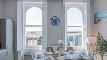 Een eetkamer met uitzicht op het strand, een klok aan de muur en een schilderij.