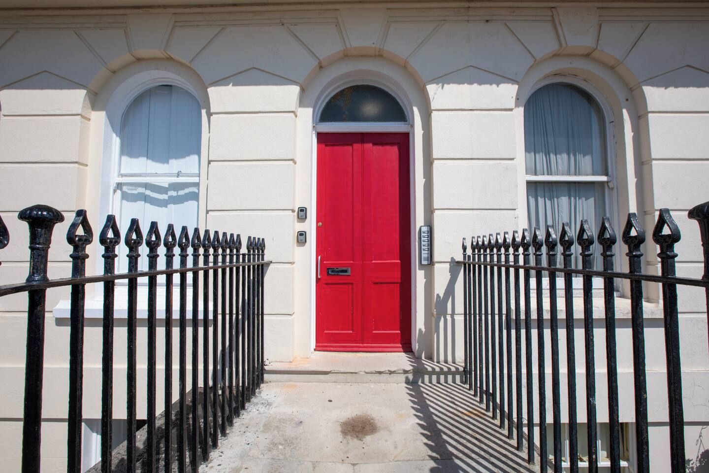A building facade with a red door, white walls, and a black iron fence.