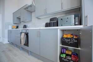 Eine moderne Küche mit grauen Schränken, einem Einbauofen, einer Kaffeemaschine und einer Snackbar mit verschiedenen Snacks und Kaffeegetränken.