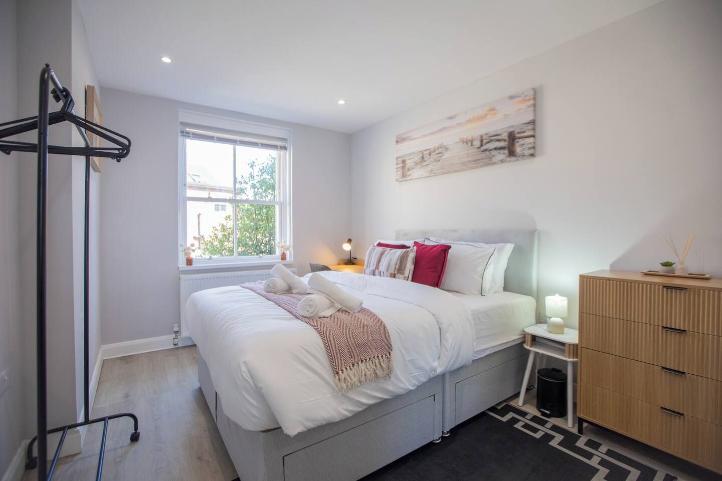 Een moderne slaapkamer met een bed, nachtkastje, dressoir en een raam.