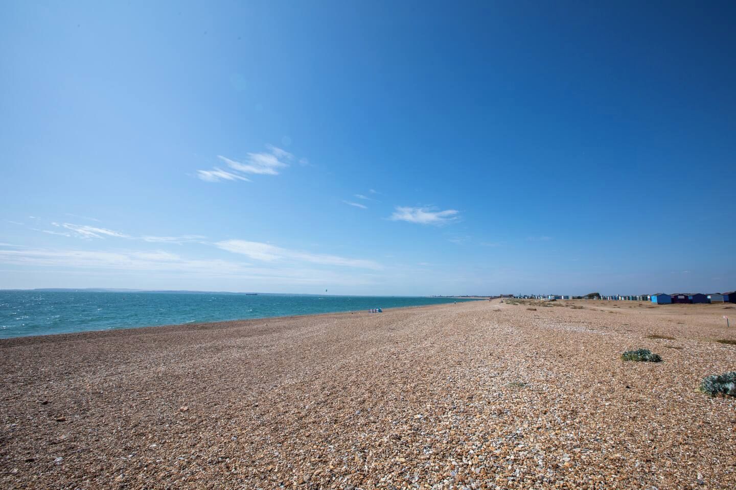 A pebbled beach with a clear sky and distant buildings.
