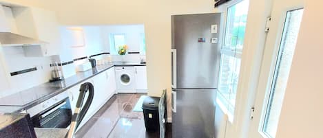 A compact kitchen with a washing machine, a refrigerator, and a window providing natural light.