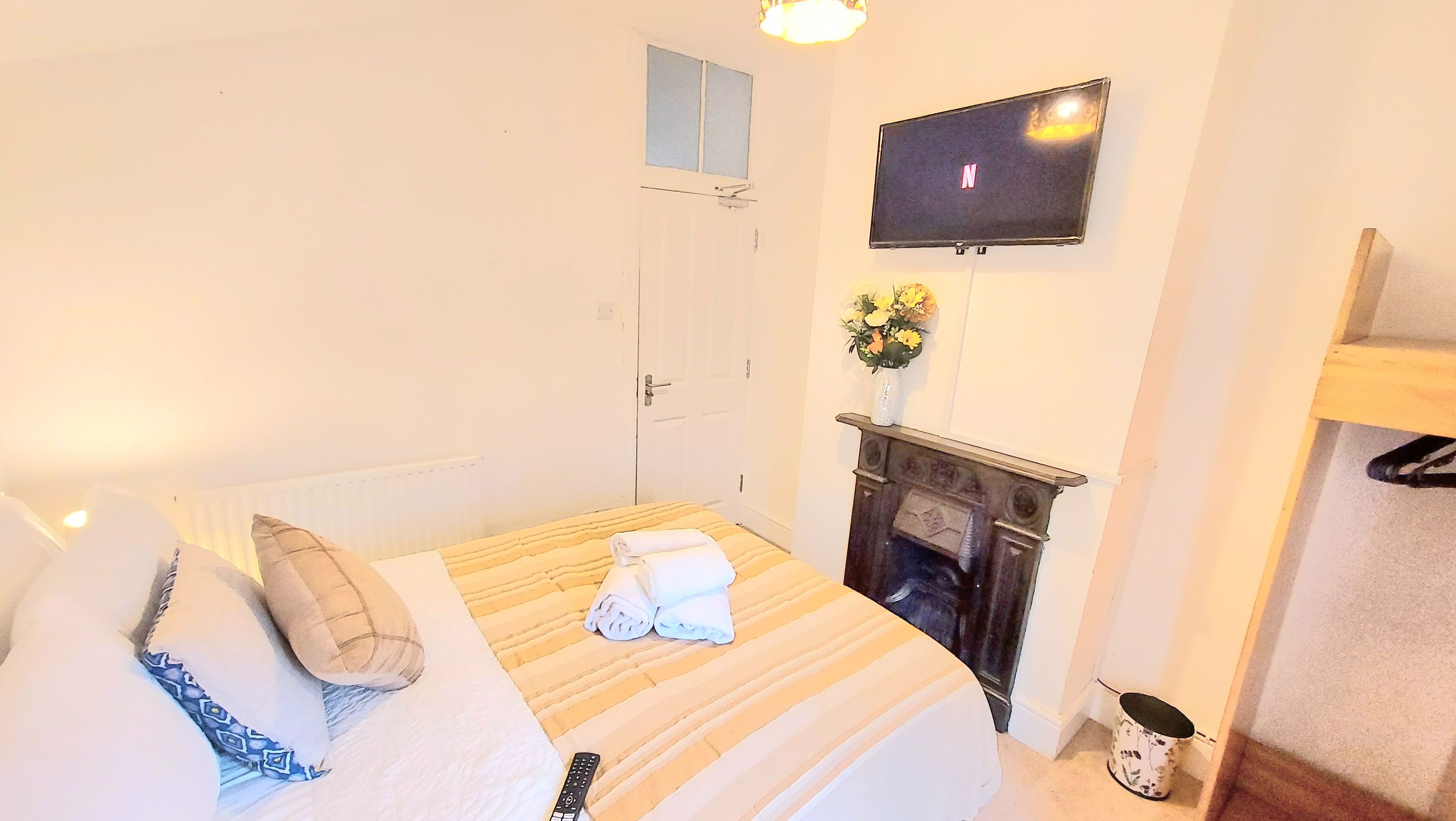 A hotel room with a bed, a flat-screen TV mounted on the wall, a fireplace, and a small window.