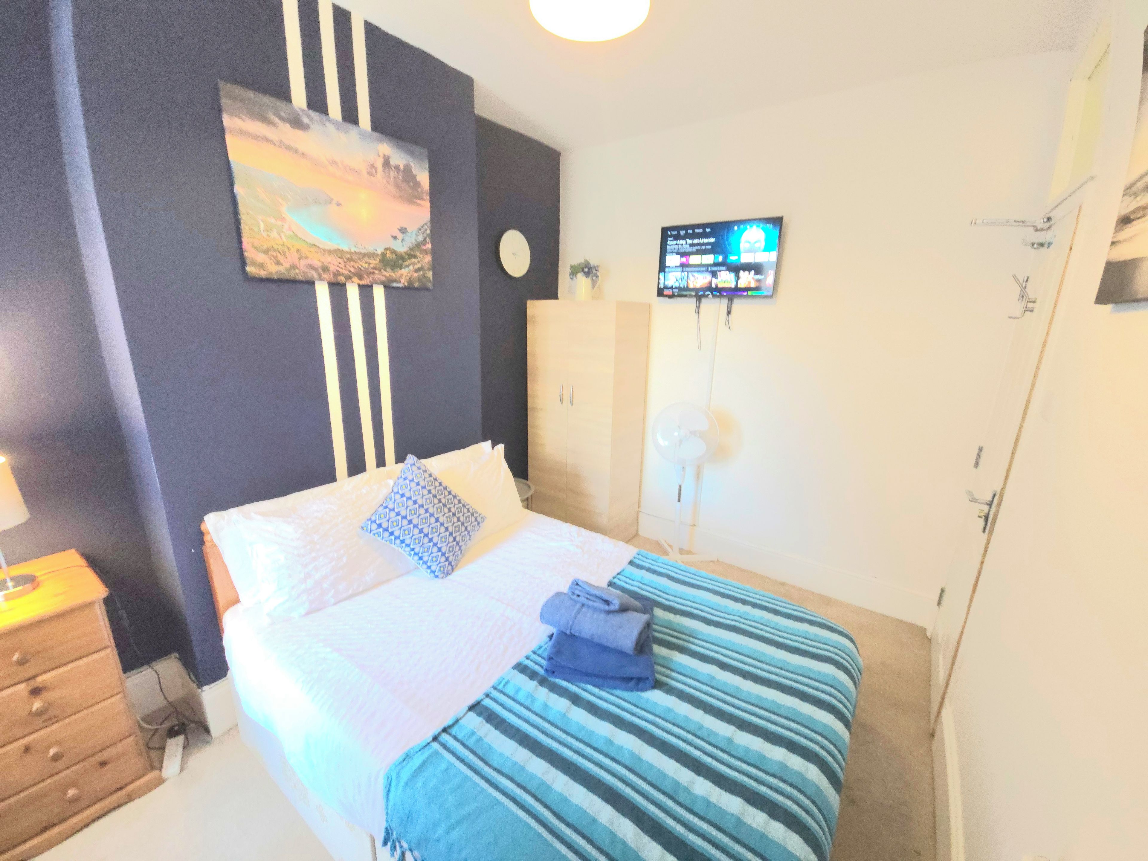 A bedroom with a bed, a wall-mounted TV, a clock, and a wardrobe.