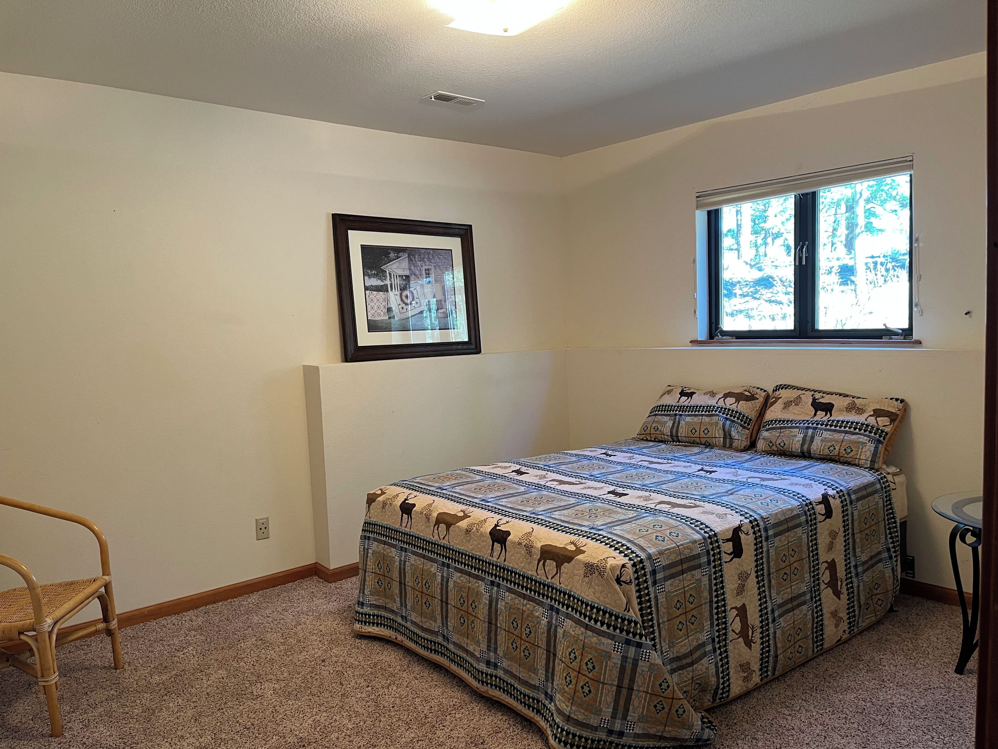 A bedroom with a bed, a chair, a window, and a framed picture on the wall.