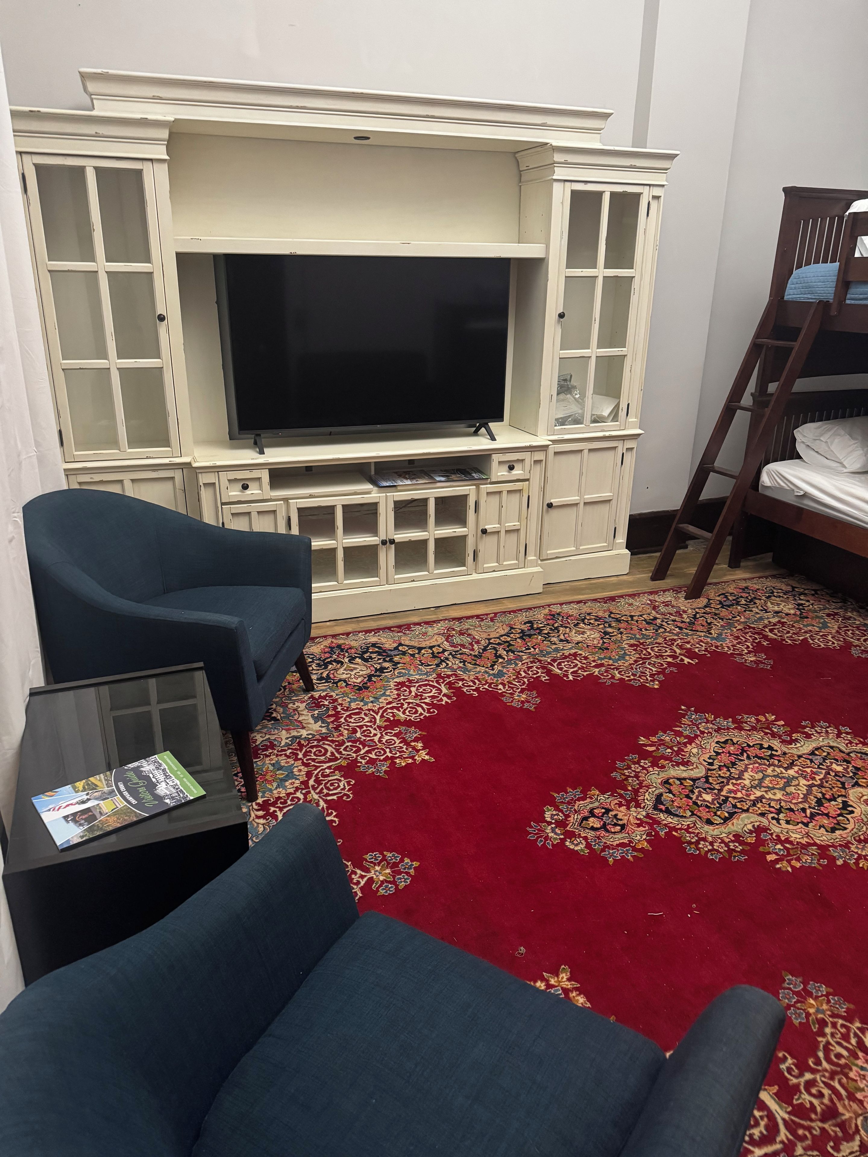 A living room with a flat-screen TV, a blue sofa, a coffee table with a magazine, and a red patterned carpet.